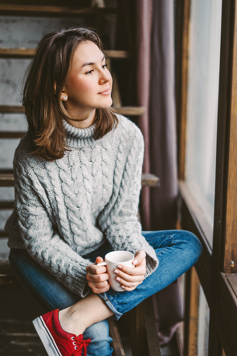 Young woman drinking coffee by the window
